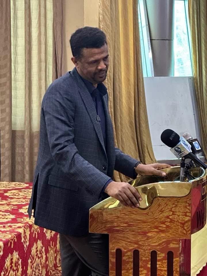 A participant speaking at a lectern in a meeting room.