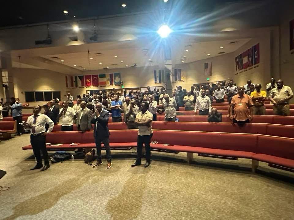 Participants seated in a large auditorium facing the stage.