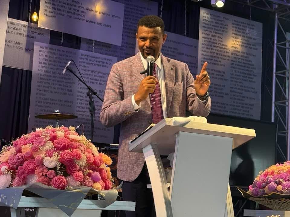 A speaker reading from a book at a lectern.